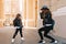 Cute little girl in black pants with holes on knees posing on the street, while her mother taking photo. Graceful young