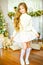 Cute little girl with blond long curly hair in a light knitted sweater by the festive fireplace with garlands