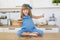 Cute little girl in blue dress sits on a table with a cake in a hand and closed eyes