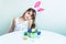 Cute little girl with bunny ears paints eggs at a white table. Easter concept