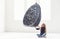 A cute little girl in casual clothes sits near a suspended chair in an empty studio.