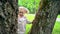 Cute little girl child hiding over tree trunk. Happy toddler playing outdoor