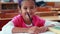 Cute little girl colouring in book in classroom smiling at camera