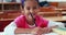 Cute little girl colouring in book in classroom smiling at camera