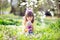 Cute little girl with curly hair wearing bunny ears and summer dress having fun during Easter egg hunt relaxing in the garden