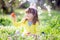 Cute little girl with curly hair wearing bunny ears and summer dress having fun during Easter egg hunt relaxing in the garden