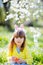 Cute little girl with curly hair wearing bunny ears and summer dress having fun during Easter egg hunt relaxing in the garden