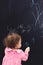 Cute little girl drawing something with chalk on blackboard