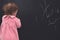 Cute little girl drawing something with chalk on blackboard