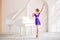 A cute little girl dreams of becoming a professional ballerina. In a white room, next to the piano, a girl in a lilac leotard is