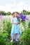 Cute little girl in dress and straw hat holds a bouquet of lupins in flowering field. Girl holds a bouquet of purple flowers in a