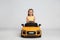 Cute little girl driving children`s electric toy car on grey background