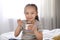 Cute little girl eating tasty yogurt on bed