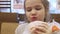 a cute little girl eats a burger and drinks soda in a cafe.