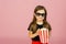 Cute little girl eats popcorn from striped packaging and watches a movie with 3D glasses. Cinema advertising concept, watching