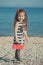 Cute little girl enjoying summer time on sea side beach happy playing with red star and tiny toy anchor on sand wearing nobby clot