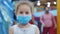 Cute little girl from an epidemic of coronaviruses or viruses looks at the camera among people in masks from the virus