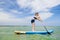 Cute little girl exercise paddling on SUP board in sea on sunny day while summer holidays