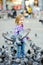 Cute little girl feeding and chasing birds on Dam Square in Amsterdam on summer day