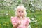 Cute Little Girl In Flowering Apple Orchard Blowing Dandelion Seeds Outside