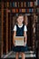 Cute little girl in glasses stands in the library full of books. Conception of education