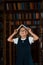 Cute little girl in glasses stands in the library full of books. Conception of education