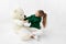 A cute little girl in green clothes hugs a Teddy bear on a white background, space for text