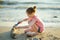 Cute little girl having fun on a sandy beach on warm and sunny summer day by the sea. Kid playing by the ocean