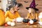 Cute little girl and her mother, both in witch costumes, sitting behind a table in Halloween theme decorated room.