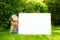 Cute little girl holding big blank whiteboard on sunny summer day outdoors