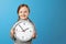 A cute little girl holding a big clock over a blue background. The concept of education, school, timing, time to learn.