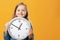 A cute little girl holding a big clock over a yellow background. The concept of education, school, timing, time to learn.