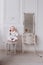 A cute little girl is holding a makeup brush and doing make up. baby Girl is sitting on the chair near the classic mirror at . Kid