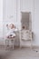 A cute little girl is holding a makeup brush and doing make up. baby Girl is sitting on the chair near the classic mirror at . Kid