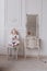A cute little girl is holding a makeup brush and having fun at home. baby Girl is sitting on the chair near the classic mirror