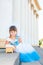 Cute little girl in a holiday white and blue dress is sitting on the steps near the columns