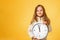 Cute little girl in a jacket holds a big clock on a yellow background. The concept of education, school, deadlines, time to study