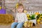 Cute little girl in jeans and white blouse playing hide and seek with a chicken sitting at a haystack close to yellow eggs and