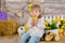 Cute little girl in jeans and white blouse playing hide and seek with a chicken sitting at a haystack close to yellow eggs and