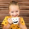 Cute little girl laughing and drinking pumpkin soup out of a cup with Halloween anthropomorphic smiley face. Halloween background.