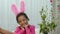 A cute little girl looks in funny pink bunny ears looks at the camera and smiles. African American child posing against