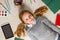 Cute little girl is lying on the floor. A child is surrounded by a book, tablet, paints, brushes, pencils