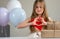 Cute little girl making heart with her hands and smiling surrounded by air balloons and gifts. Adorable kid smiling in