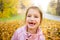 Cute little girl with missing teeth playing with yellow fallen leaves in autumn forest.