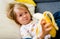 Cute little girl o sofa eating pealed banana and looking towards camera with smile and full mouth