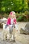 Cute little girl petting and feeding a goat at petting zoo. Child playing with a farm animal on sunny summer day.