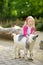 Cute little girl petting and feeding a goat at petting zoo. Child playing with a farm animal on sunny summer day.