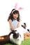 Cute little girl with pink bunny ears playing with rabbits on green grass. Joyful kid holding her pet and celebrating Easter day