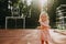 Cute little girl in pink casual dress smiling standing on sports court at sunset.