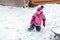Cute little girl in pink sport suit having fun playing outdoors during snowfall in winter. Children winter seasonal outdoor